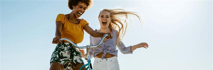 Two girls playing with a bicycle on the boardwalk on a seaside holiday.